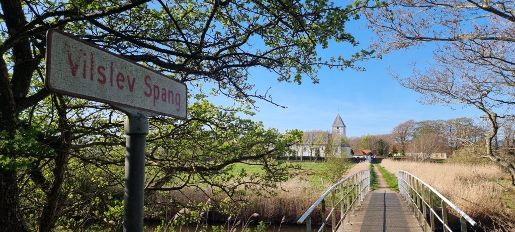 Hvid landsbykirke i baggrunden og en gangbro forrest i billedet